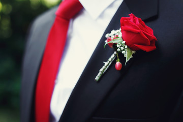 Handsome groom in black suit and red tie with red rose boutonnie