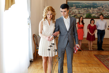 Fototapeta premium stylish beautiful blonde bride with elegant handsome groom lighting candle in registry