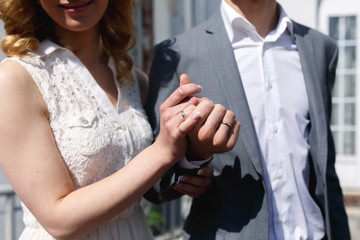 Happy stylish blonde bride and handsome groom holding hands rings close-up