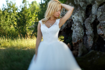 Fototapeta na wymiar Gorgeous stylish blonde wife in white dress posing in front of tree in field