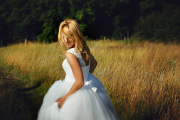 Fototapeta na wymiar Beautiful smiling stylish blonde bride walking and posing in rye field