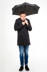 Amusing young man standing and feeling cold under umbrella