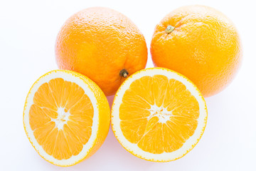 Close up photo of two cut-in-half slices of orange, with two whole oranges behind. The background is isolated.
