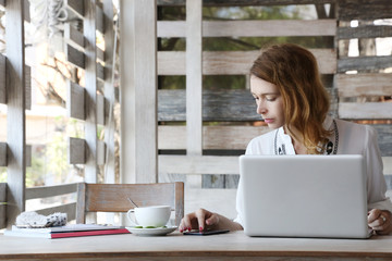 Multitasking.
Young woman using mobile phone and laptop while drinking tea