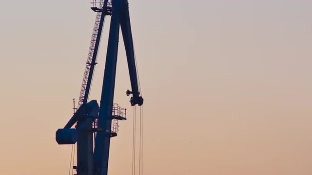 Close up of a silhouetted harbor crane loading freight during golden hour