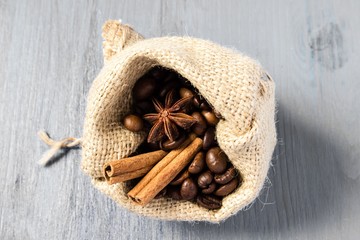 Coffee beans, star anise and cinnamon in bag on gray wooden table