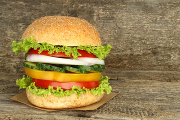 Healthy vegan burger with raw vegetables on old wooden background.
