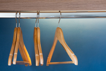 Close up of wooden hangers inside a blue closet with selective focus on the stainless pin.