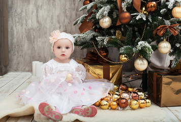 Little girl in a smart dress sits near a Christmas tree