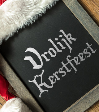 Merry Christmas (in Dutch) written on blackboard with santa hat