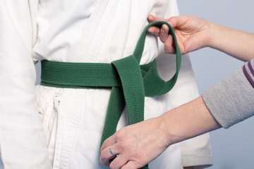 Hands of a parent who helps a child to tie a green belt