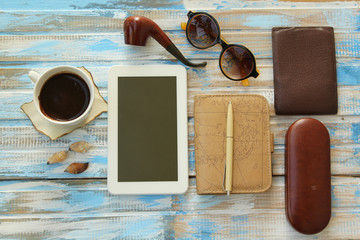 Top view of office table top with coffee cup, notebook planner, pen, tablet computer, wallet, sunglasses and case and smoking pipe
