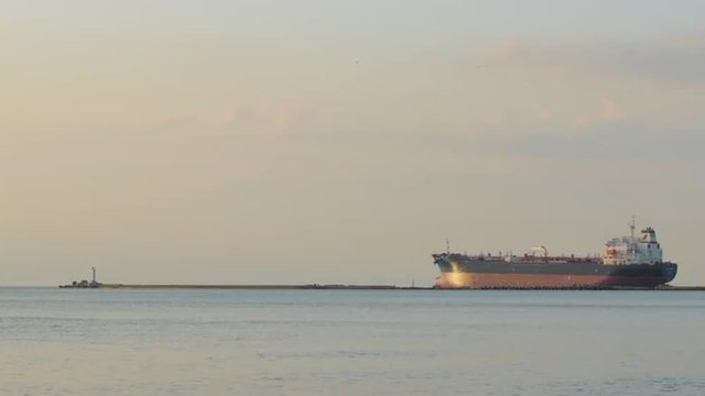 Empty bulk carrier leaving port behind a breakwater during summer sunset
