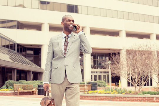 smiling business man talking on mobile phone holding briefcase walking down the street