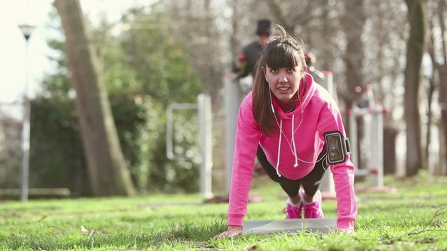 Young woman doing push ups exercises at park
