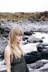 Blond woman in gray dress on rocks, looking away