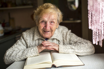 An elderly woman sits with a book at the table.