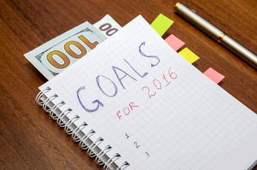 Notebook with text goals of year 2016 with dollar on wooden