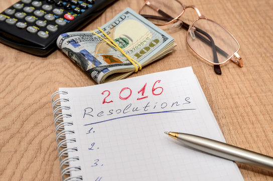 goals of year 2016 write on notebook with pen and dollars on wooden background
