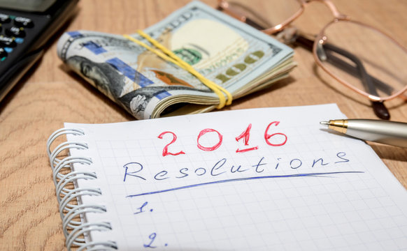 goals of year 2016 write on notebook with pen and dollars on wooden background