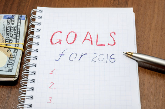 goals of year 2016 write on notebook with pen and dollars on wooden background