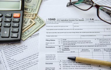 federal income tax return IRS 1040 documents with pen, calculator, dollars