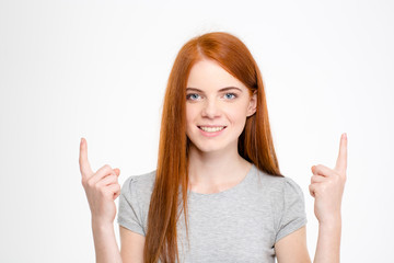 Happy cheerful redhead young woman with long hair pointing up