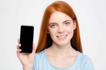 Charming cheerful young redhead woman showing blank screen of smartphone