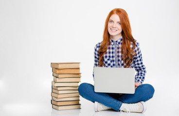 Obraz premium Happy woman sitting near stack of books and using laptop