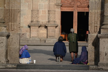 Dos señoras pobres piden limosna y dos oran en el atrio de la iglesia.