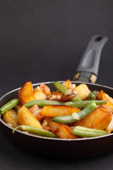 fried potatoes with green beans and bacon in a frying pan