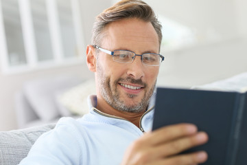 40-year-old man relaxing in sofa reading book