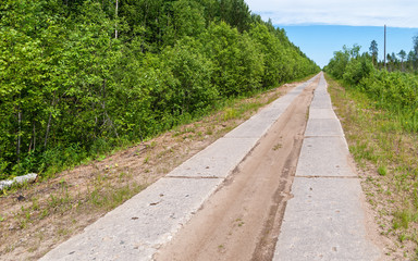 Straight road made of concrete pavement plates surrounded by green forest recedes into the distance under cloudscape blue sky. Arkhangelsky region, Russia.
