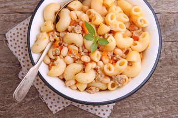 pasta with meat and beans in a white bowl on the old wooden background
