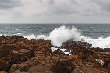 Sea wave breaking on the rocks with foam and spray. Storm wave.