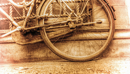 old bicycle rear wheel against a rustic wall in sepia tone