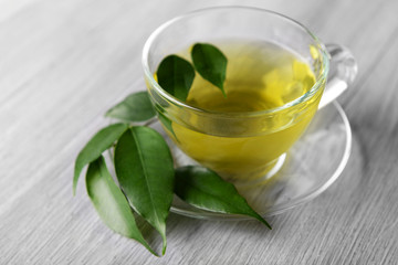 Glass cup of tea with green leaves on grey wooden background
