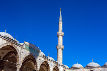 Fototapeta na wymiar Main Minaret of Blue Sultan Ahmed Mosque from inner garden with domes and gate. Daylight blue sky