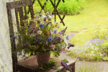 Raindrops on glass . Blurred background with a bouquet of summer flowers and a garden .
