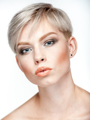 Obraz premium Closeup studio portrait of a young beautiful platinum blonde short-haired woman looking surprised with smokey blue eyes and warm natural makeup