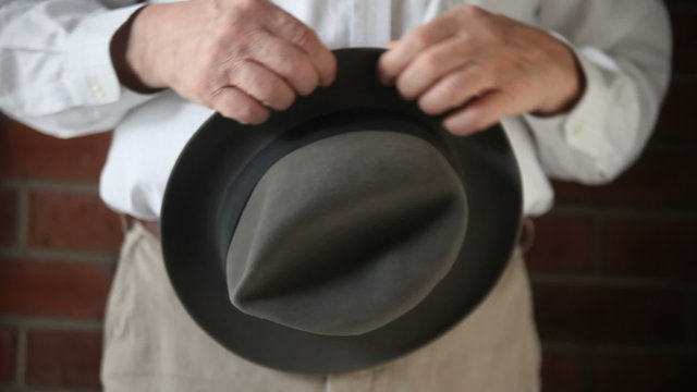 A man nervously turns an old hat in his hands.