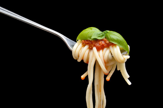 Spaghetti wound on fork with basil leaf on black background