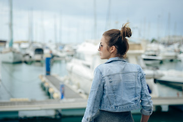 Side view of pretty girl standing on embankment with boats