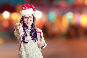 Picture of beautiful young lady in Santa Claus hat on abstract festive background design pointing finger and holding present box