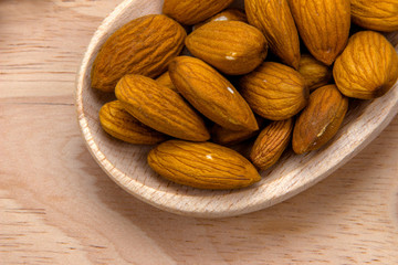 Wooden spoon with unpeeled almonds on wooden board