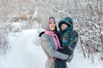 Fototapeta na wymiar Beautiful young mother walking with her son in the winter forest.