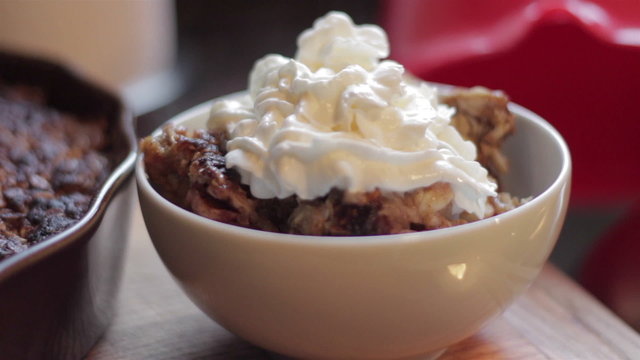 Closeup of female hand picking up a hot bowl of homemade apple crisp topped with whipped cream