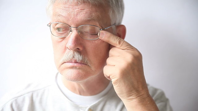 Senior man takes off his glasses to rub his very tired eyes.