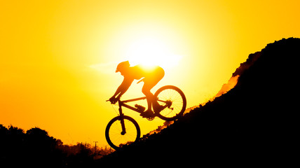 Fototapeta na wymiar A cyclist riding down the hill with sunset silhouette