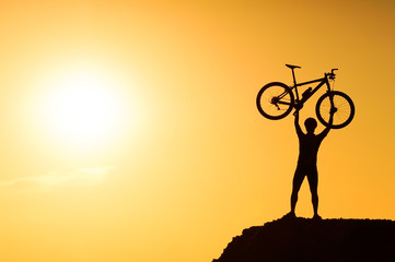 silhouette of a mountain bike cyclist standing on the mountain raising his bike